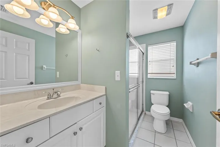 Bathroom featuring vanity, walk in shower, tile patterned floors, and toilet