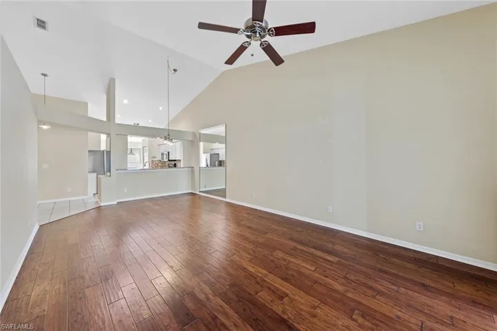 Unfurnished living room with ceiling fan with notable chandelier, hardwood / wood-style flooring, and high vaulted ceiling