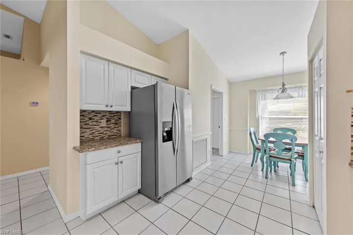 Kitchen featuring white cabinets, stainless steel refrigerator with ice dispenser, decorative light fixtures, and vaulted ceiling