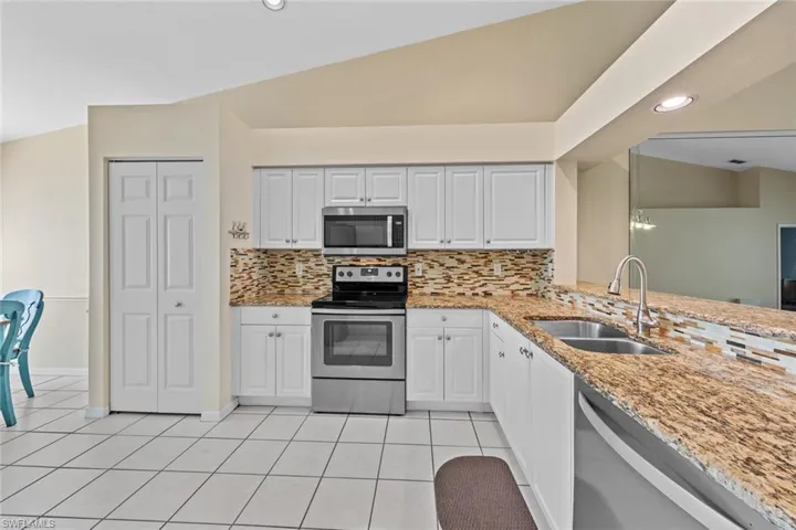 Kitchen with lofted ceiling, white cabinets, sink, backsplash, and appliances with stainless steel finishes