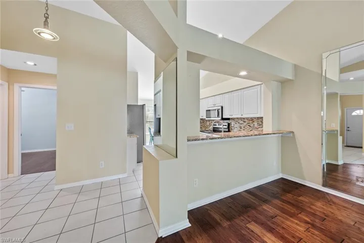 Kitchen featuring light hardwood / wood-style floors, white cabinetry, kitchen peninsula, appliances with stainless steel finishes, and decorative light fixtures