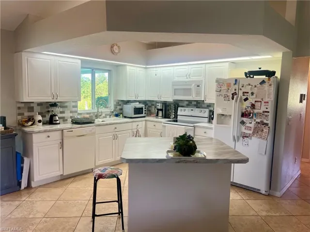 Kitchen with white appliances, sink, decorative tile backsplash, light tile patterned flooring, and white cabinetry