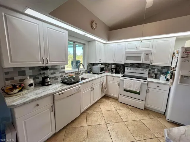 Kitchen featuring white cabinets, tiled backsplash, white appliances, and sink