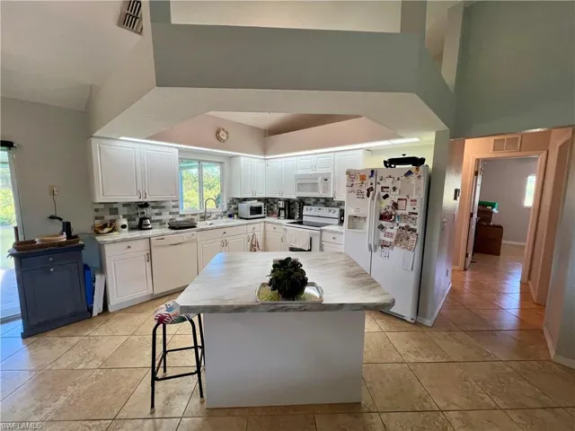 Kitchen featuring white appliances, white cabinets, sink, tile backsplash, and a kitchen island