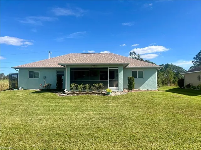 Rear view of property featuring a screened lanai and a yard