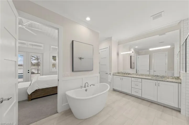Ensuite bathroom featuring double vanity, a soaking tub, wainscoting, and crown molding New CUSTOM MIRROR & SCONCES (February 2020), New WALLPAPER (June 2020), New PRIMARY BATH CEILING PAINT (July 2023)