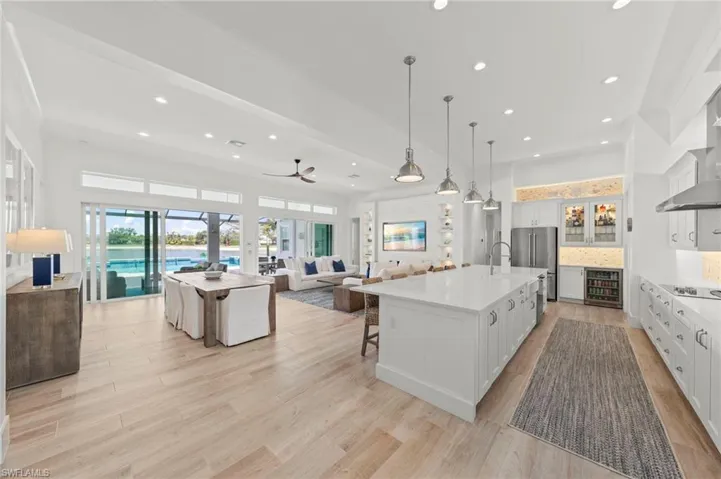 Kitchen featuring open floor plan, a kitchen island with sink, decorative light fixtures, white cabinets, and a kitchen breakfast bar New MOUNTED TV & SONOS SOUND BAR (November 2018), New KITCHEN PENDANTS (November 2018), New SHIPLAP BUILT-IN & WALLS (May 2020), New KITCHEN INTERIOR PAINT (July 2023), new CEILING FAN (October 2024)