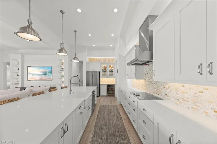 Kitchen with white cabinets, hanging light fixtures, decorative backsplash, light wood-style floors, and high end refrigerator New KITCHEN PENDANTS (November 2018), New WINE REFRIGERATOR (November 2018), New KITCHEN INTERIOR PAINT (July 2023)