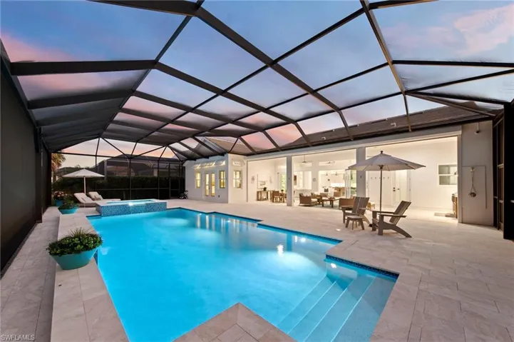 Pool at dusk with a sunroom, a pool with connected hot tub, a patio area, and a lanai