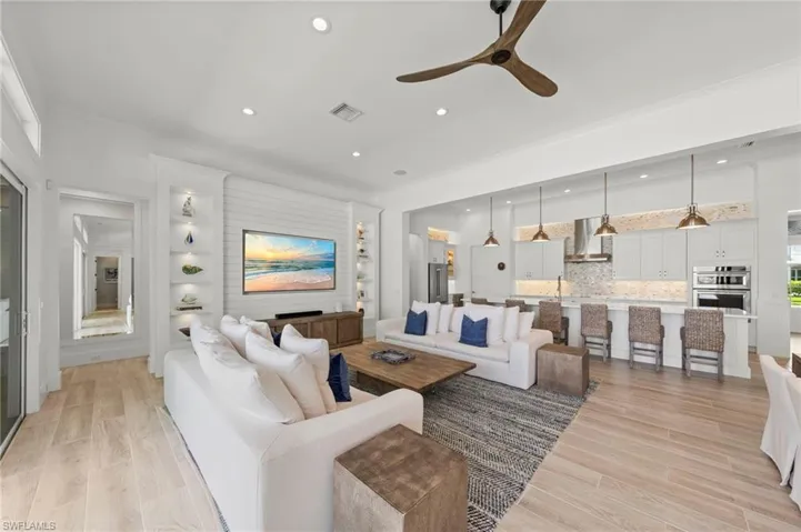 Living room featuring crown molding, wood tiled floors, ceiling fan, recessed lighting, and built in features New MOUNTED TV & SONOS SOUND BAR (November 2018), New KITCHEN PENDANTS (November 2018), New SHIPLAP BUILT-IN & WALLS (May 2020, New KITCHEN INTERIOR PAINT (July 2023)New CEILING FAN (October 2024)