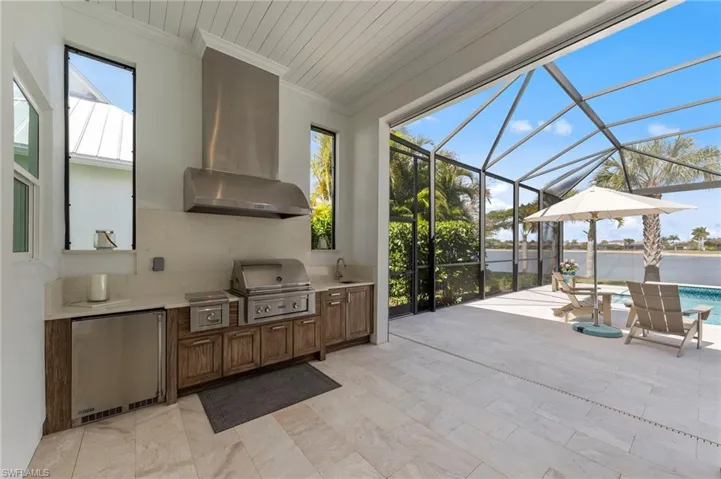 View of patio with glass enclosure, area for grilling, a sunroom, an outdoor pool, and a water view New OUTDOOR KITCHEN (December 2018), New electric Storm Smart HURRICANE SHUTTERS (March 2019), New SHIPLAP CEILING & CROWN MOLDING (May 2020),