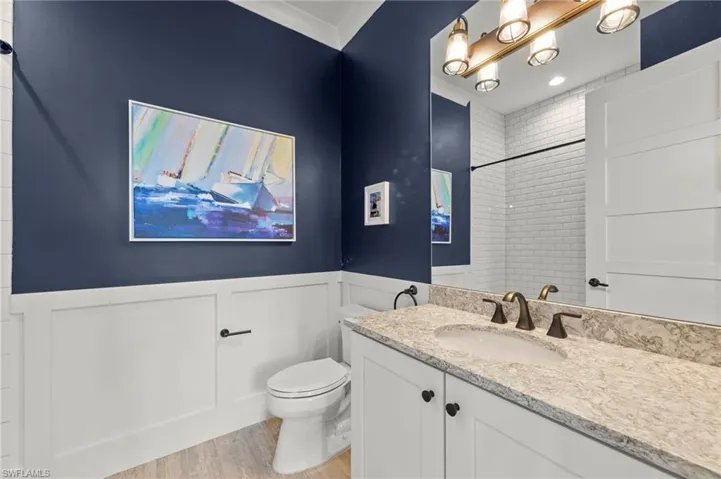 Bathroom with vanity, light wood-style flooring, a wainscoted wall, a shower, and a decorative wall