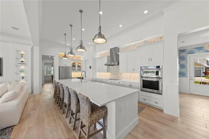 Kitchen featuring a breakfast bar area, white cabinetry, light wood-style floors, a large island, and decorative light fixtures New KITCHEN PENDANTS (November 2018), New KITCHEN INTERIOR PAINT (July 2023)