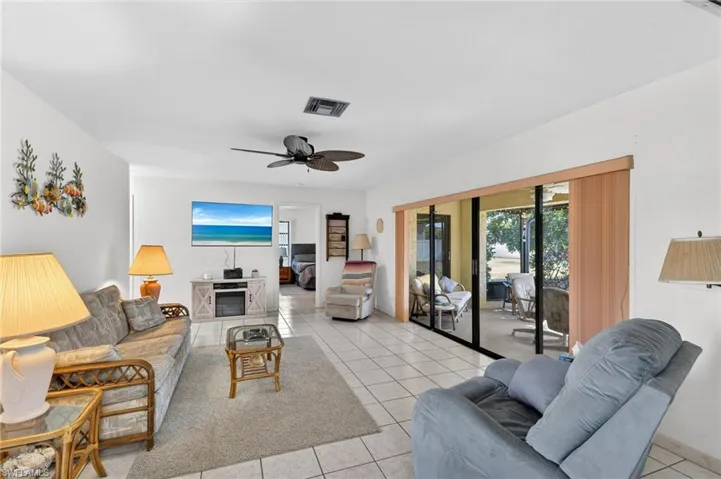 Spacious living area featuring tile flooring, a ceiling fan, and sliding glass doors opening to an enclosed patio
