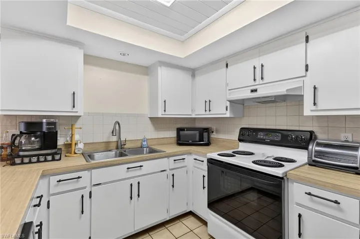 Kitchen featuring abundant white cabinetry, light wood-finish countertops, and a full-size white electric range with a black cooktop