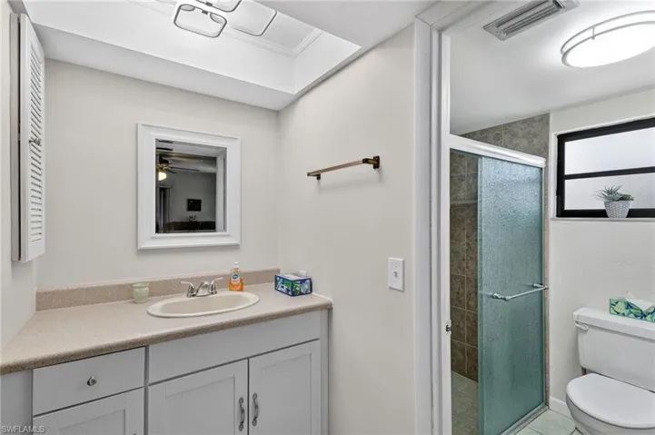 Bathroom featuring a single vanity with a laminate countertop, white cabinetry, a framed mirror, and an enclosed shower with tile surround