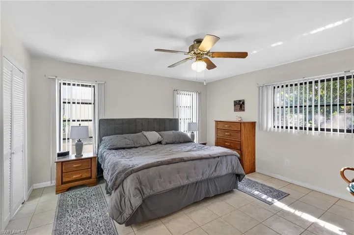 Spacious room featuring light-colored tile flooring, multiple windows with vertical blinds, and a ceiling fan with integrated lighting