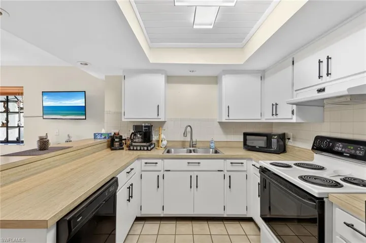 Kitchen featuring white cabinetry with black hardware, wood-finish countertops, and a white tile backsplash
