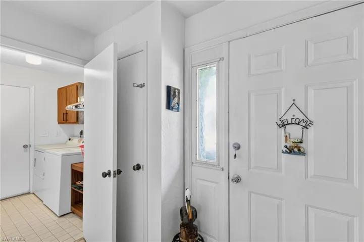 Entryway with a paneled door, sidelight, and tiled flooring, providing access to a utility space featuring a washing machine, storage cabinets, and a flat-panel ceiling light