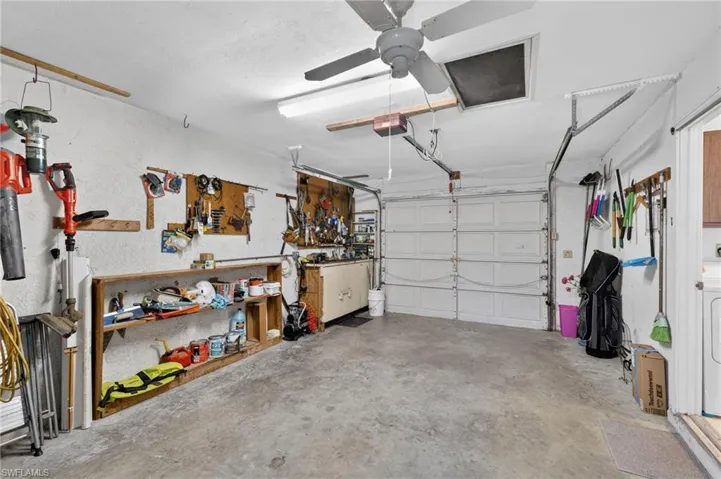 Spacious garage featuring a concrete floor, built-in shelving, attached ceiling fan, and overhead fluorescent lighting