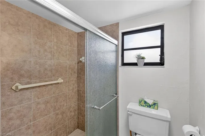 Tiled shower enclosure with a sliding frosted glass door, featuring a built-in grab bar and a black-framed window