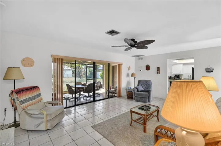Spacious living area featuring light-toned tile flooring, a ceiling fan, and large sliding glass doors opening to an enclosed patio