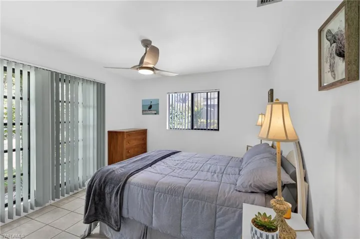 Bedroom featuring large sliding glass doors with vertical blinds, a window with horizontal blinds, and a ceiling fan with integrated lighting