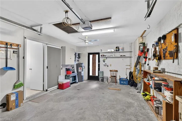 Spacious garage featuring a concrete floor, built-in shelving, overhead lighting, an attic access panel, and an attached water heater