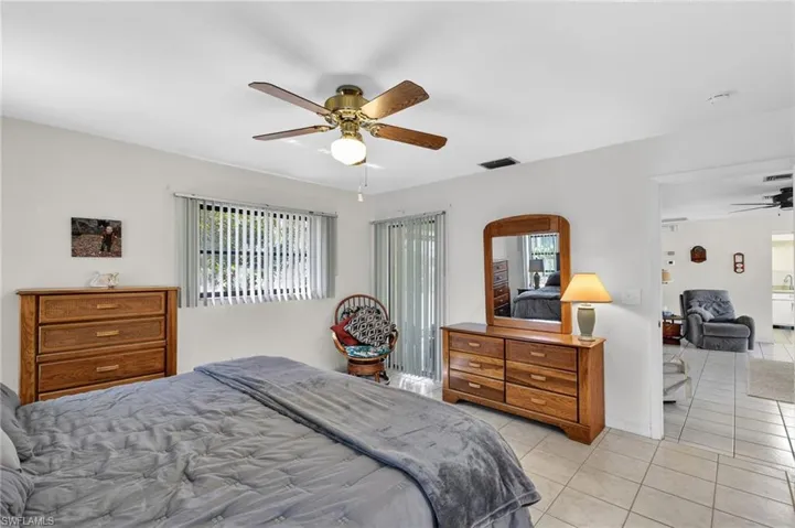 Bright bedroom space featuring a ceiling fan with integrated lighting, a window with vertical blinds, and tile flooring