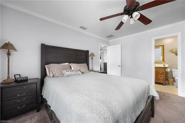 Bedroom with light carpet, ornamental molding, ensuite bath, and a ceiling fan