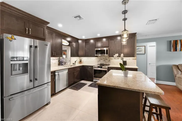 Kitchen with stainless steel appliances, light stone counters, a center island, tasteful backsplash, and crown molding