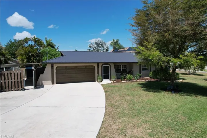 Ranch-style home with an attached garage, concrete driveway, a front lawn, stucco siding, and a metal roof