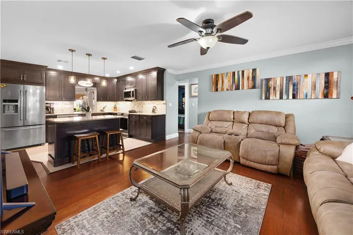Living room with ornamental molding, dark wood-type flooring, and a ceiling fan