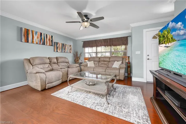 Living area with ornamental molding, dark wood-type flooring, and a ceiling fan