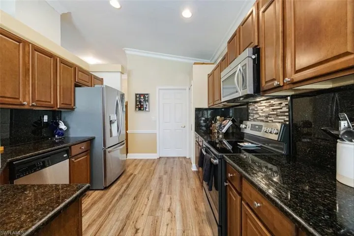 Kitchen featuring crown molding, stainless steel appliances, backsplash, light wood finished floors, and brown cabinets