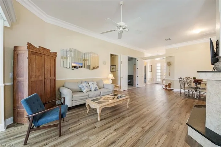 Living area with light wood-type flooring, baseboards, ceiling fan, and ornamental molding