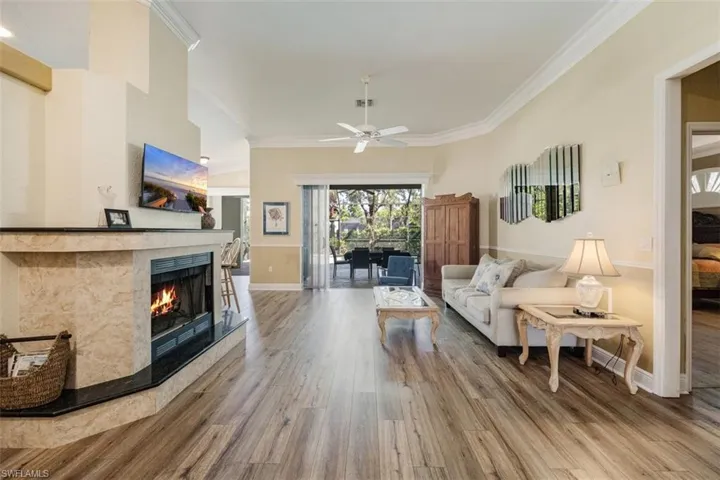 Living area with crown molding, a tiled fireplace, wood finished floors, baseboards, and ceiling fan