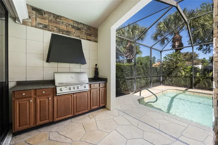 View of pool with a grill, glass enclosure, exterior kitchen, and a patio area