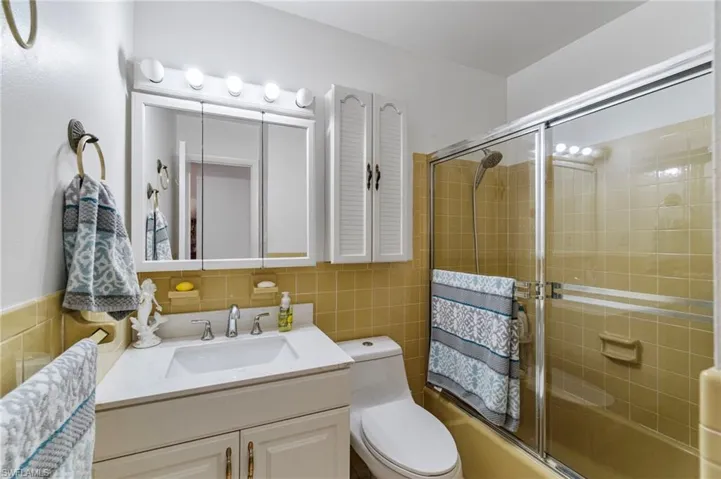Full bathroom featuring vanity, bath / shower combo with glass door, tile walls, and tasteful backsplash
