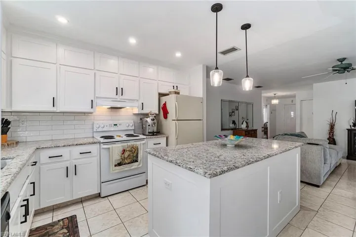 Kitchen with white cabinetry, white appliances, a kitchen island, and recessed lighting