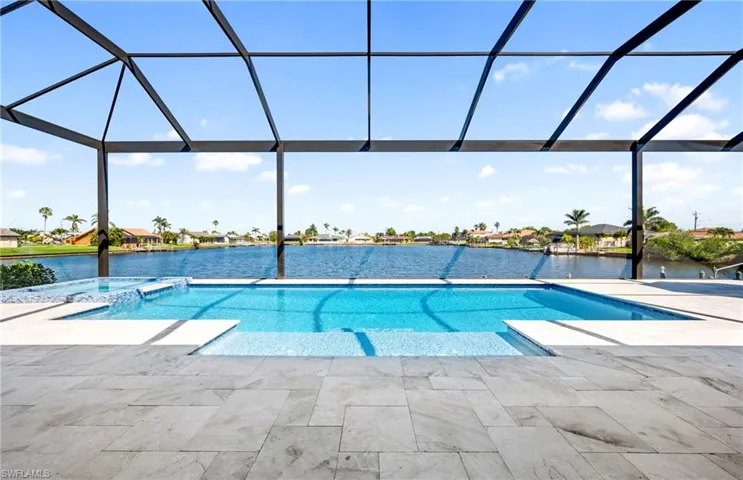View of pool featuring glass enclosure, a patio area, a water view, and a pool with connected hot tub