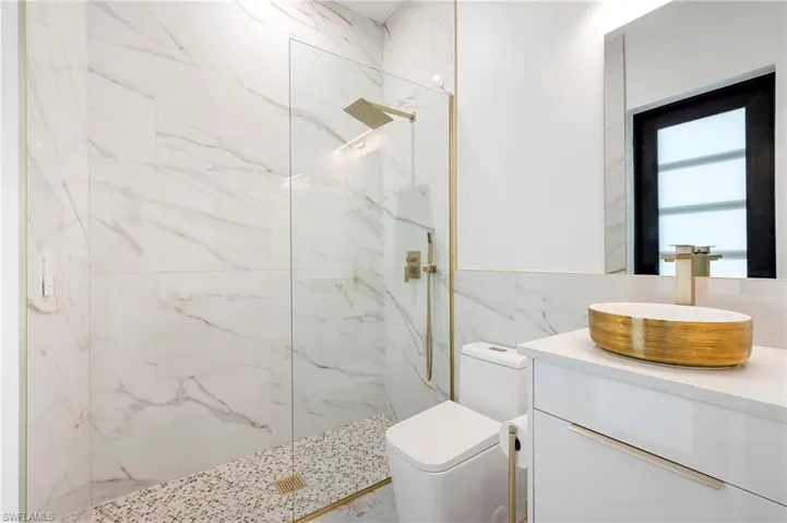 Bathroom featuring a marble finish shower, toilet, tile walls, and vanity