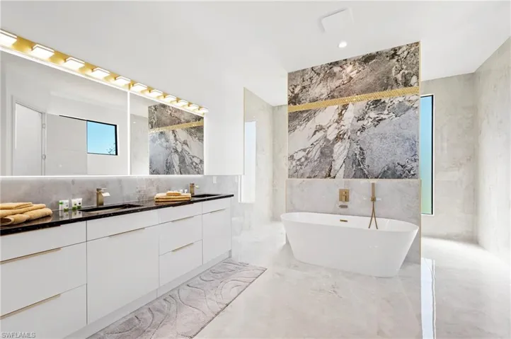 Bathroom with a freestanding bath, double vanity, marble finish floor, tile walls, and a sink