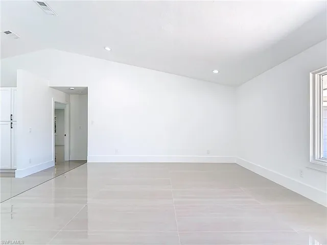 Empty room featuring vaulted ceiling, light tile patterned flooring, and recessed lighting