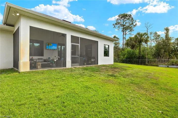 Rear view of house featuring fence, stucco siding, a sunroom, and a lawn