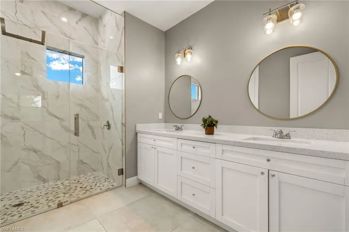Bathroom with a sink, tile patterned floors, a marble finish shower, and double vanity
