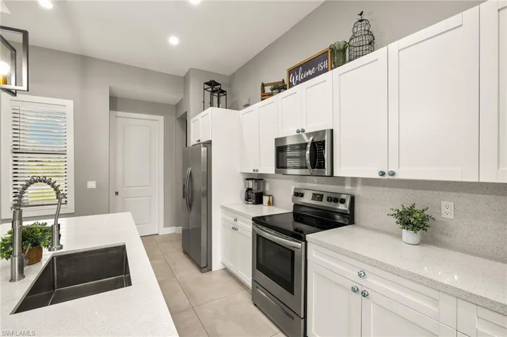 Kitchen featuring light tile patterned floors, white cabinetry, a sink, stainless steel appliances, and backsplash