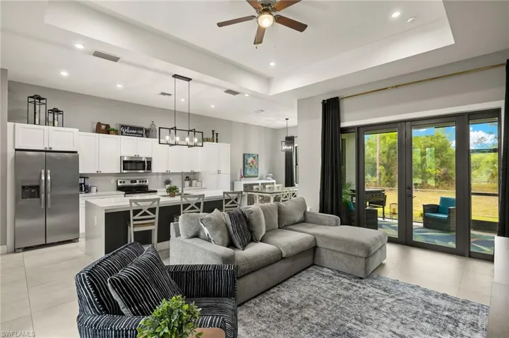 Living room with ceiling fan with notable chandelier, light tile patterned flooring, and a raised ceiling
