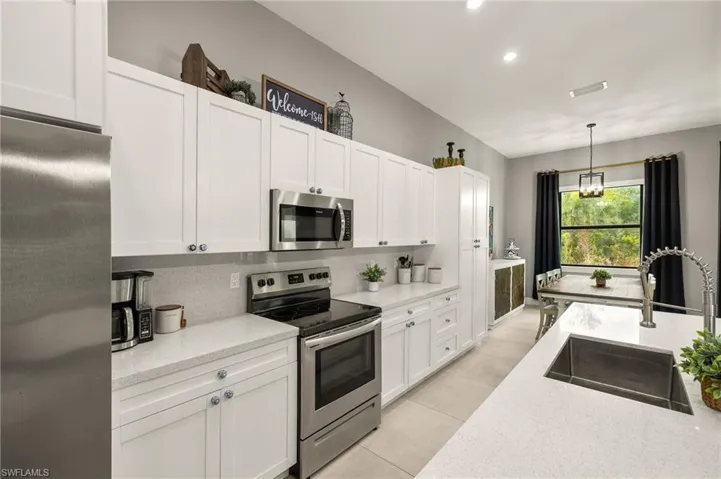 Kitchen with white cabinets, a sink, appliances with stainless steel finishes, backsplash, and pendant lighting