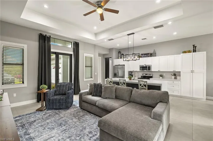 Living area featuring visible vents, a raised ceiling, light tile patterned floors, and a ceiling fan